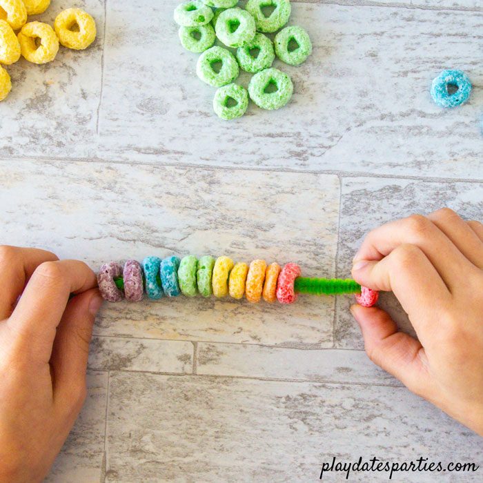 Making rainbow cupcake toppers Step 2: Add cereal to a pipe cleaner in rainbow order
