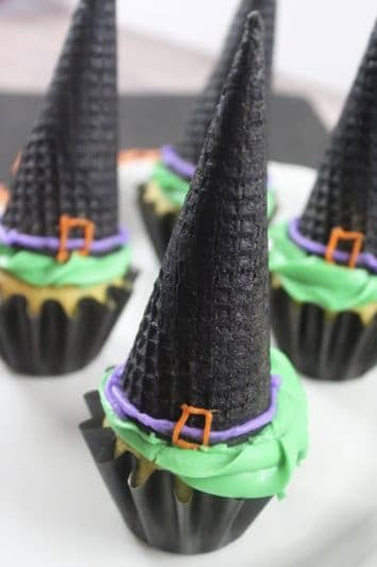 cupcakes with green frosting and black ice cream cones that look like witches hats as a Halloween party snack