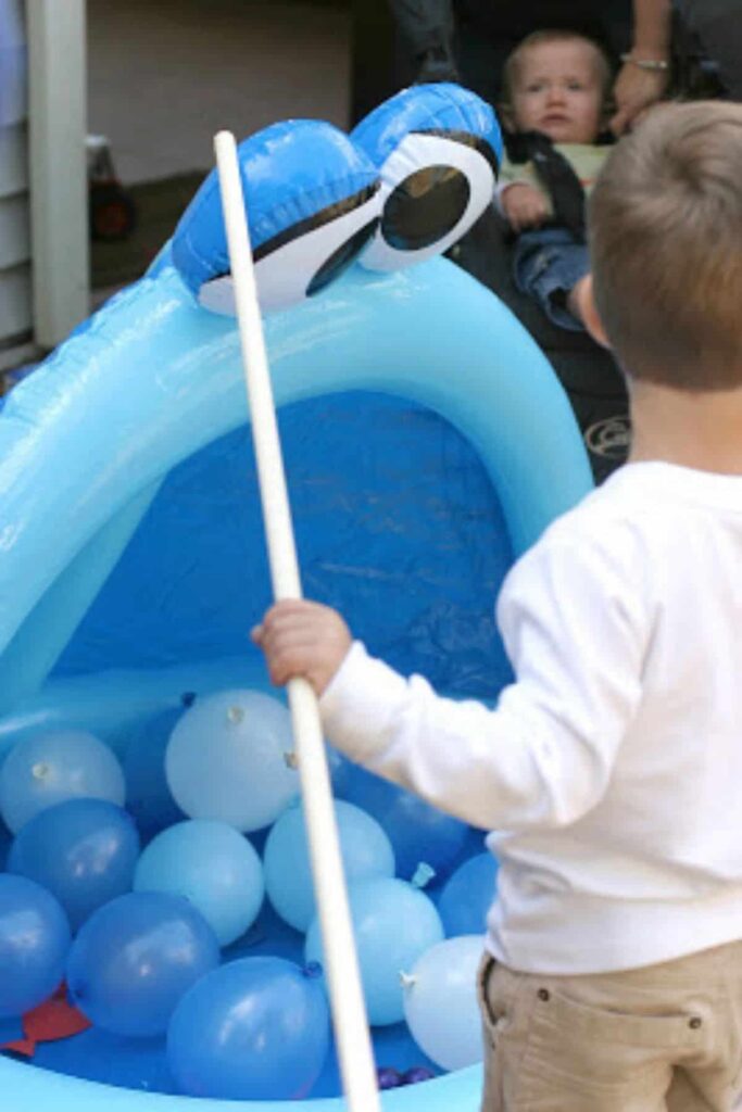 toddler playing a party game in an inflatable pool filled with balloons