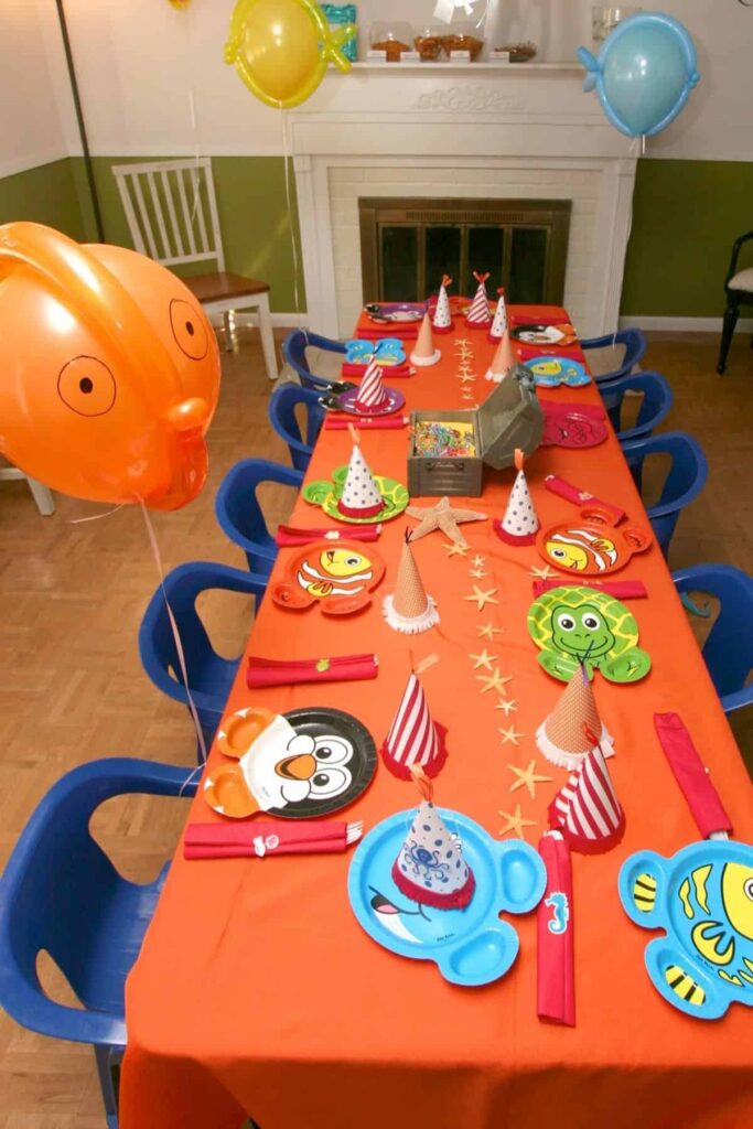 overhead view of a birthday party table for kids with an orange tablecloth and blue chairs