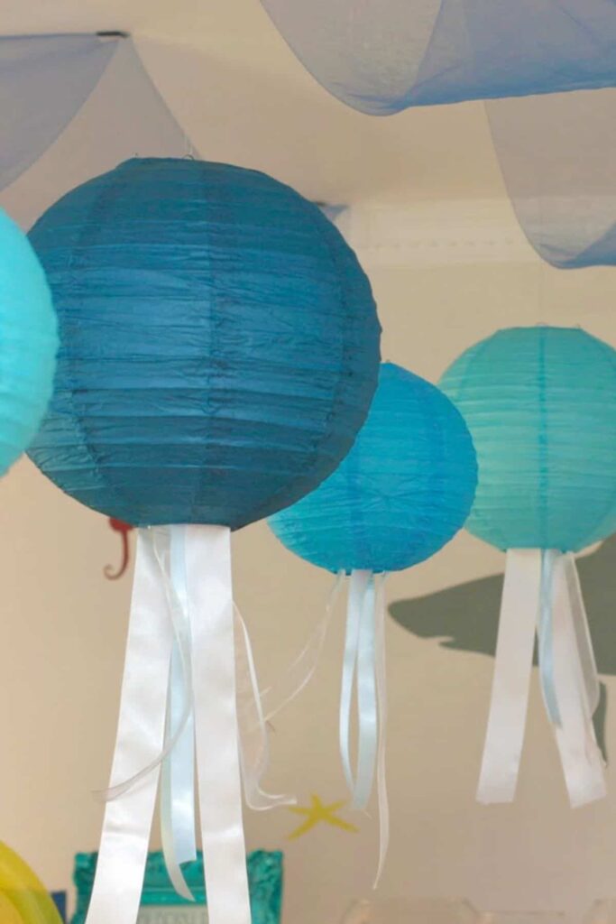 paper lanterns hanging from a ceiling with ribbons to look like jellyfish tentacles