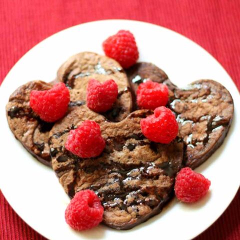 Heart shaped chocolate pancakes on a plate with fresh raspberries.