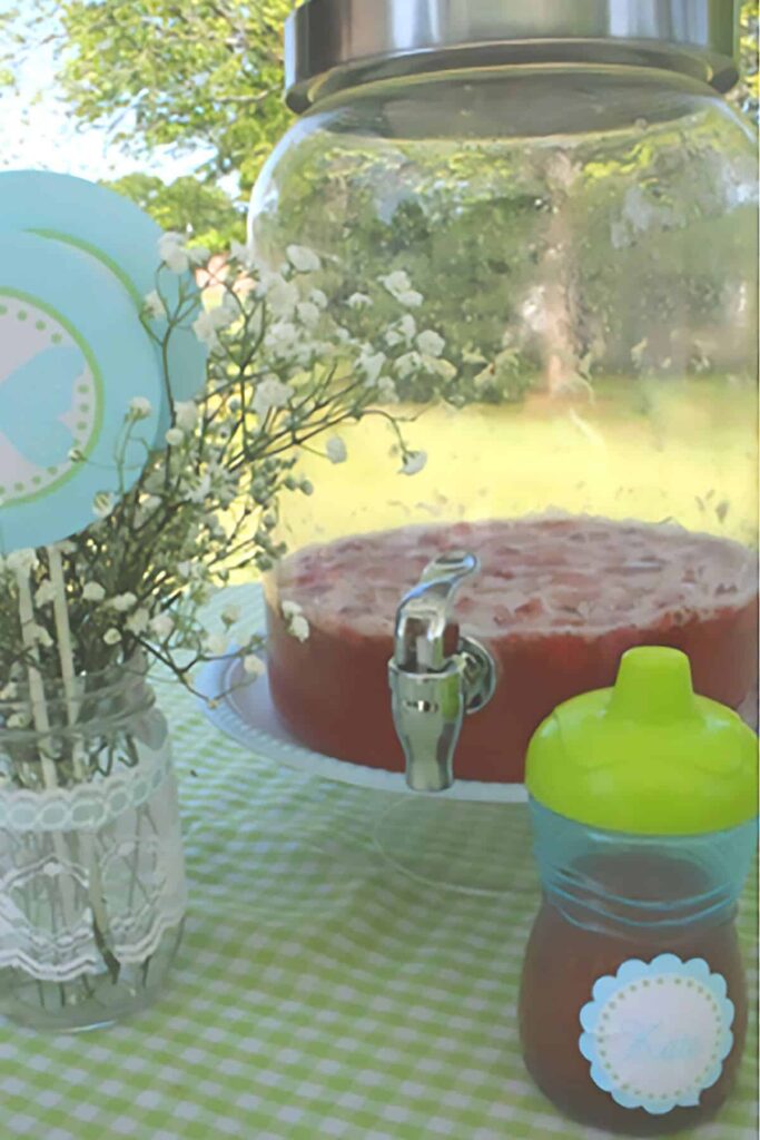 glass punch pitcher on a table with a vase of baby's breath and a sippy cup in front