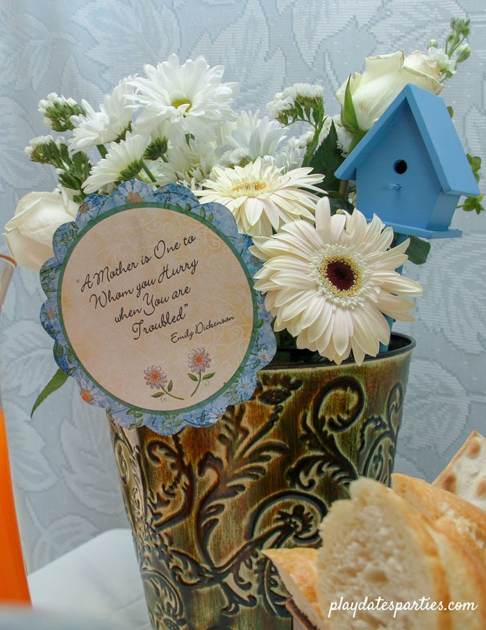 White flowers in a green vase with blue accents, and a card with the quote "A Mother is One to whom you hurry when you are troubled" by Emily Dickenson