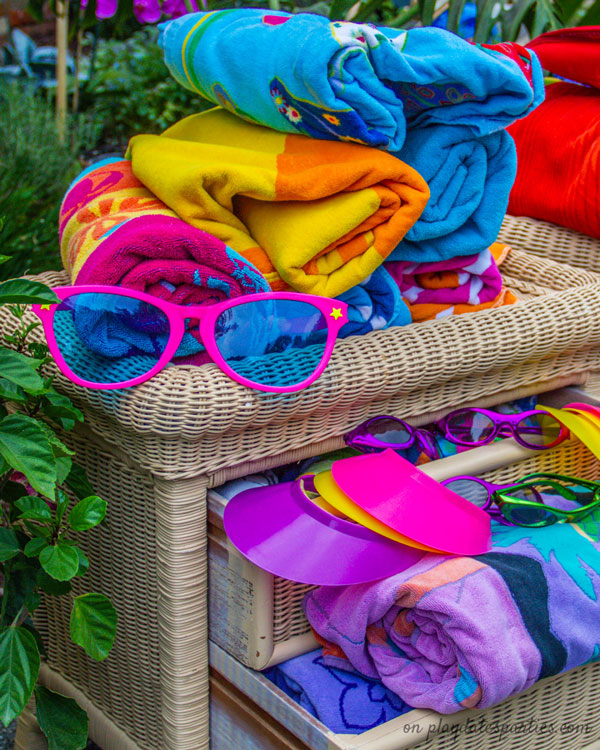 Beach towels, sun visors, and giant sunglasses displayed on a rattan dresser.