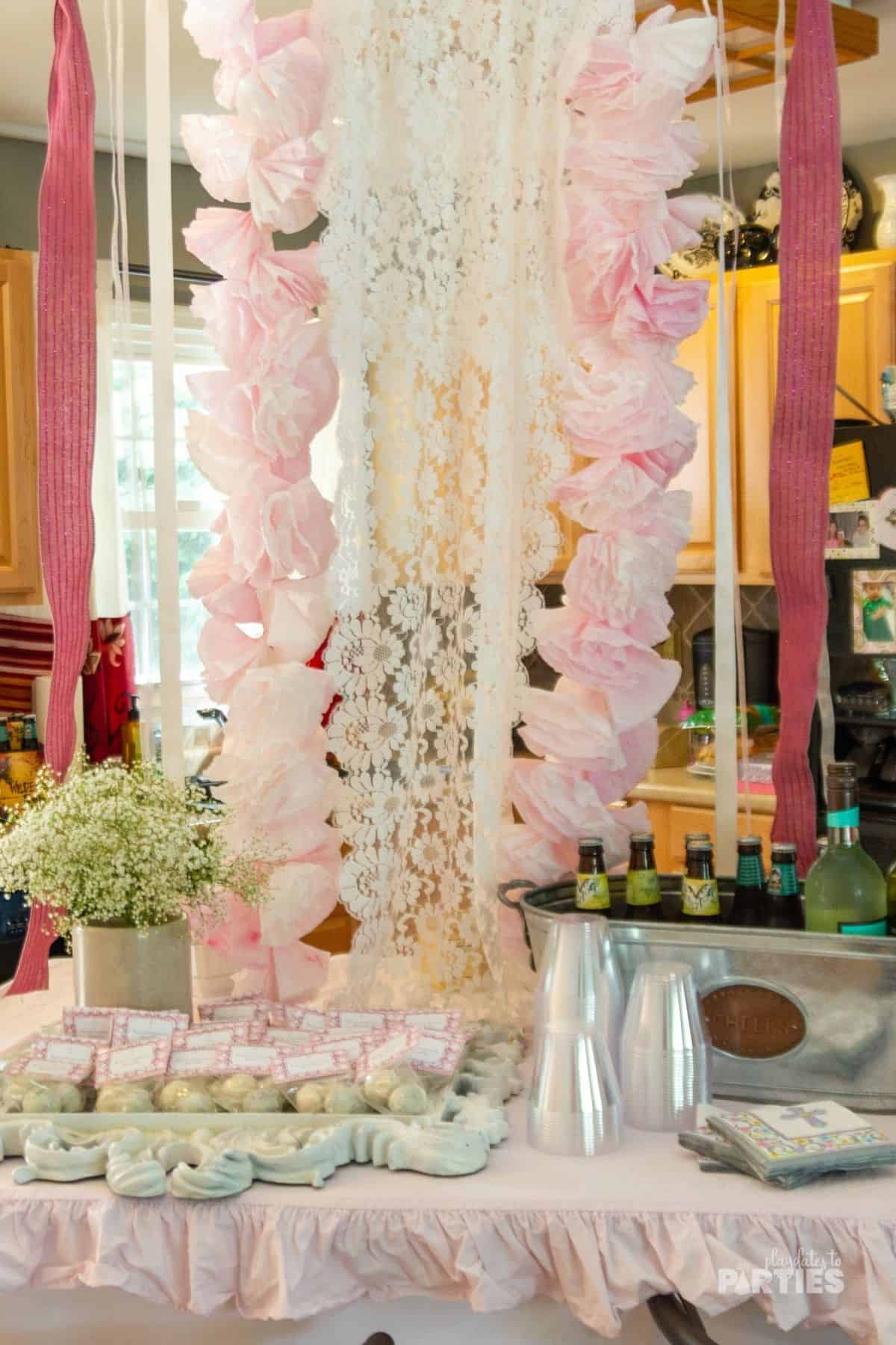 Pink ribbons and lace hang from the ceiling as a bacdrop behind the party drinks and favors.