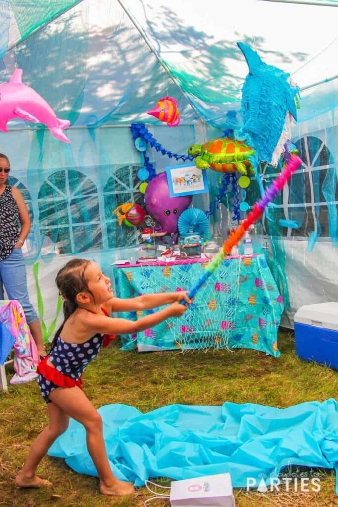 a little girl hitting a shark pinata inside a party tent