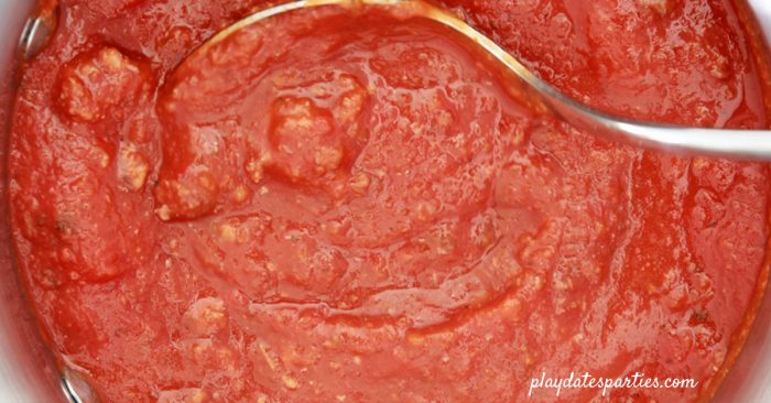 A pot full of healthy pasta sauce with a ladle in the middle.