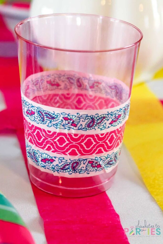 a pink tinted clear plastic cup wrapped with blue and pink washi tape on a table decorated with crepe paper streamers