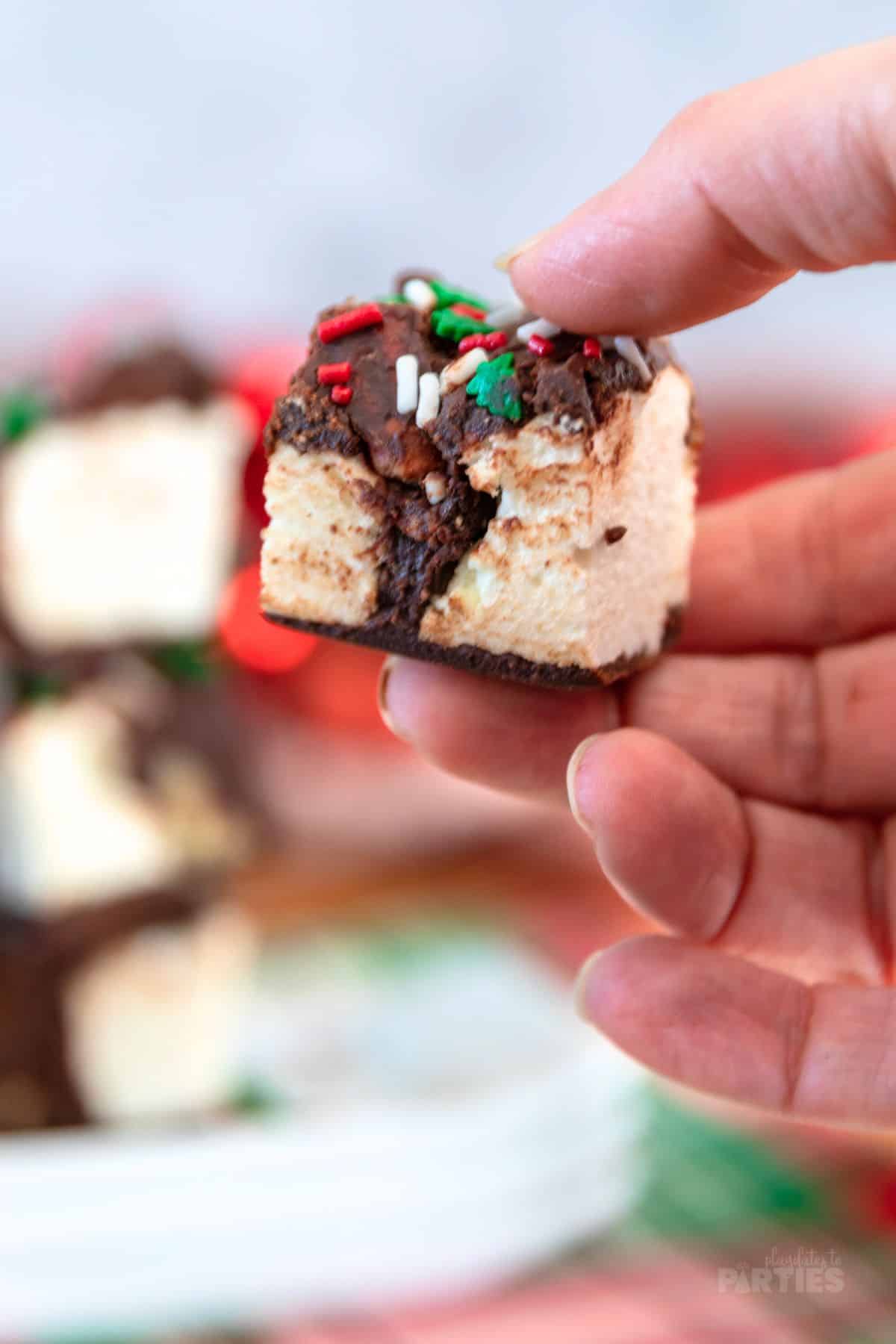 A woman's hand holding a square of chocolate covered marshmallow candy.