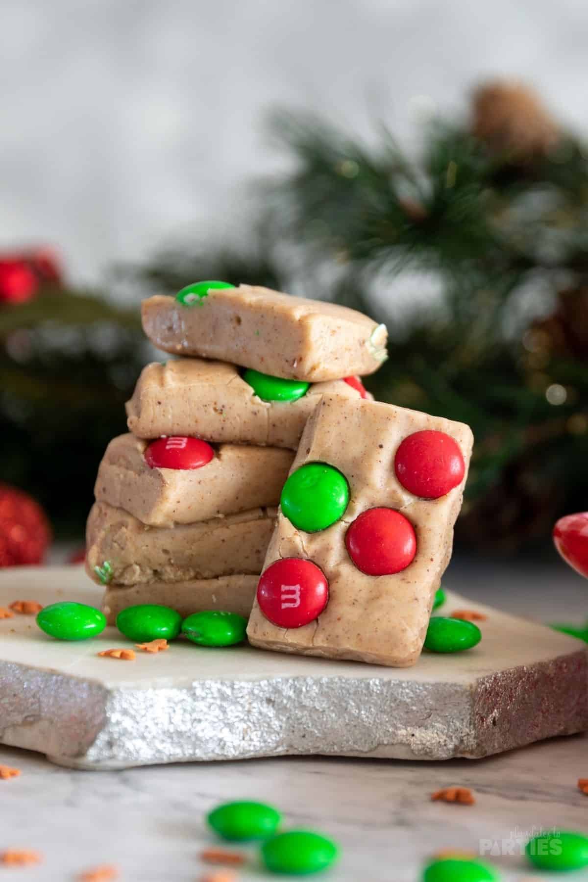5 pieces of Gingerbread fudge stacked up with candy scattered nearby.
