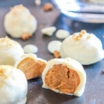 Pumpkin pie truffles on a baking sheet. One truffle is cut in half to expose the pumpkin cream cheese center.
