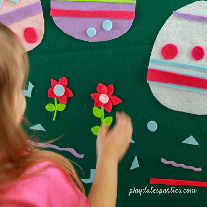 A little girl combining felt shapes to create flowers on a green felt board