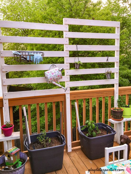 The deck privacy screen with plants hanging off the slats, and gardening supplies hanging off of s-hooks from the slats