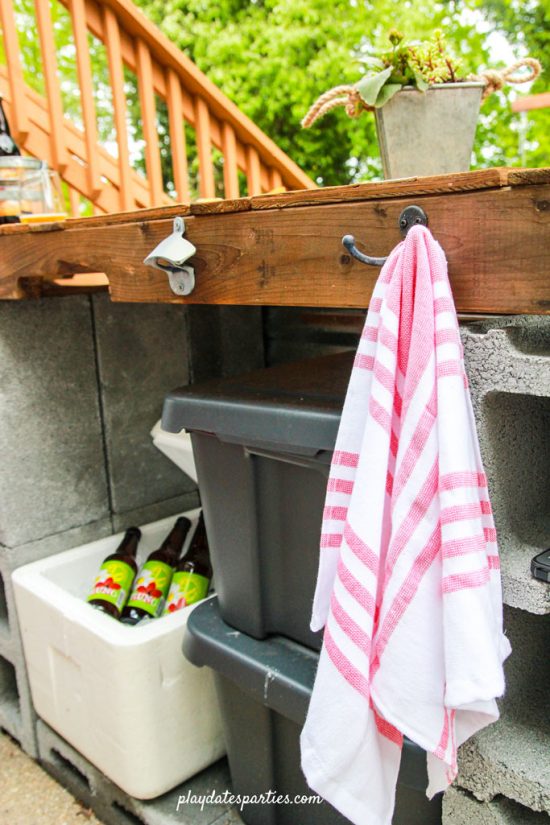 DIY outdoor bar showing a bottle opener, cooler, and towel hooks.