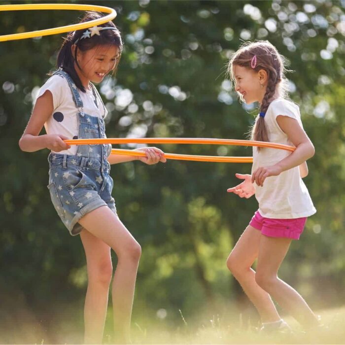 two girls playing outside with a hula hoop