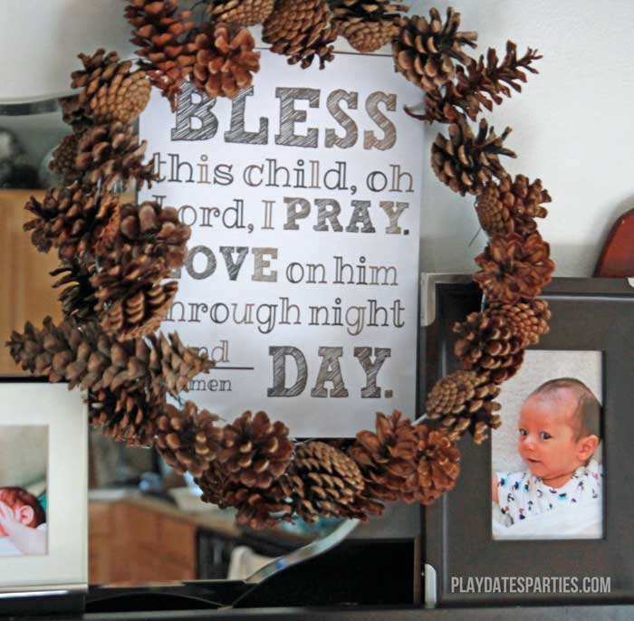 This pine cone wreath surrounds a custom print at a brown and white, fall inspired baptism for a baby boy.