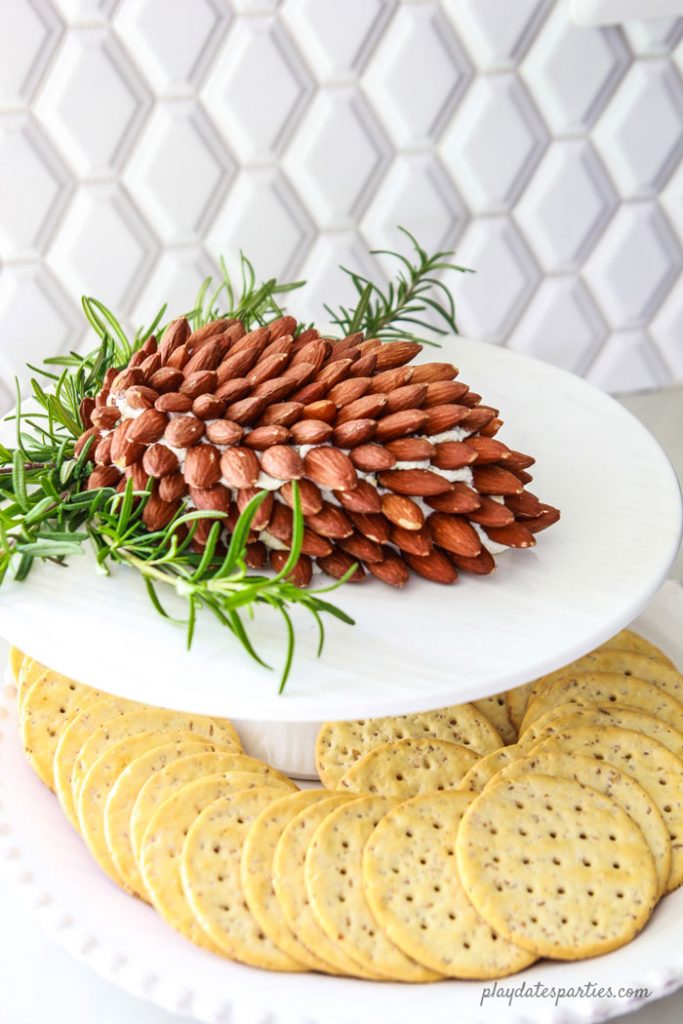 cheese ball on a small cake stand sittting on a plate of crackers