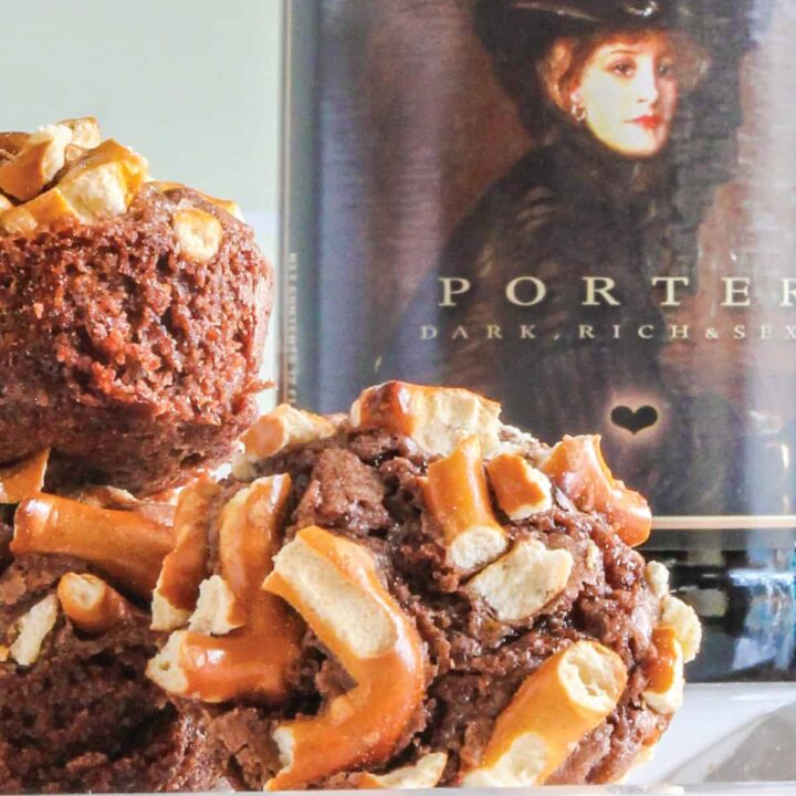 close up off a brownie bite with pretzel topping on a white plate in front of a bottle of beer