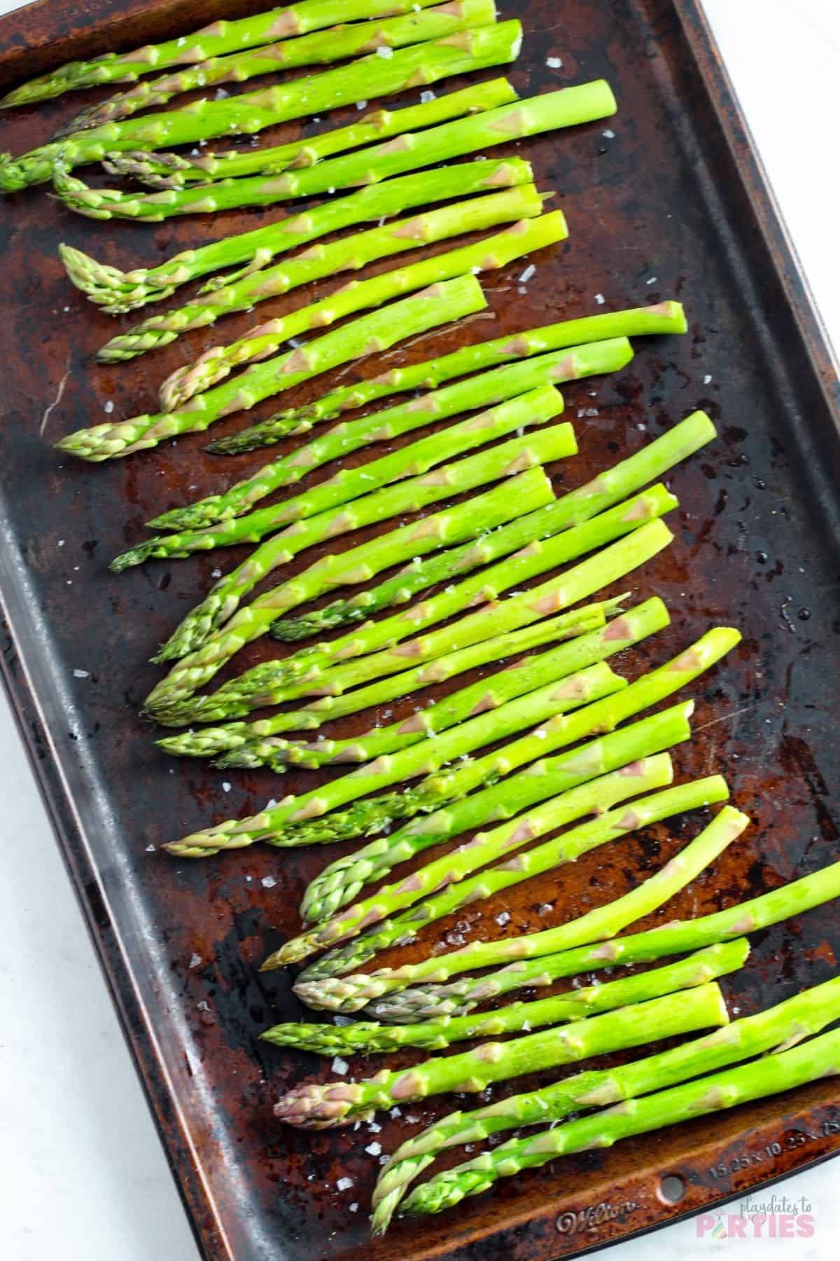 Overhead view of seasoned asparagus spears on a baking sheet.
