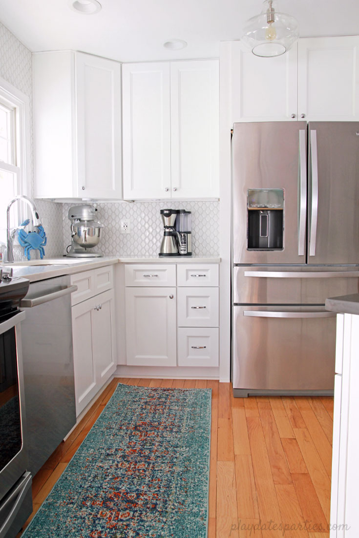 Big style can fit in #small spaces! Take a look at how this small white kitchen renovation turned a broken-down #kitchen into an updated, bright, and classic room. This home #design includes faux marble quartz countertops, DIY wood shelves, light wood floors, and modern white tile.