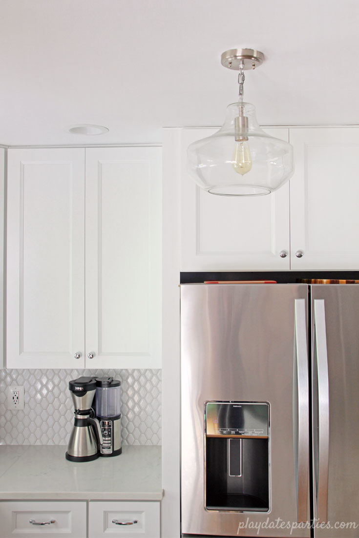 Small white kitchen, big on style. Faux marble #quartz countertops, beveled #white #tile backsplash, and a clear glass urn pendant add charm to this neutral home #design.