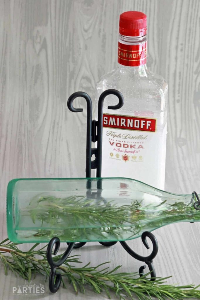 a bottle of vodka behind a partially filled bottle with a rosemary sprig inside