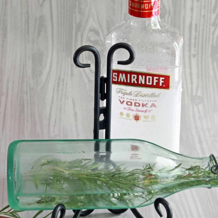 a bottle of vodka behind a partially filled bottle with a rosemary sprig inside