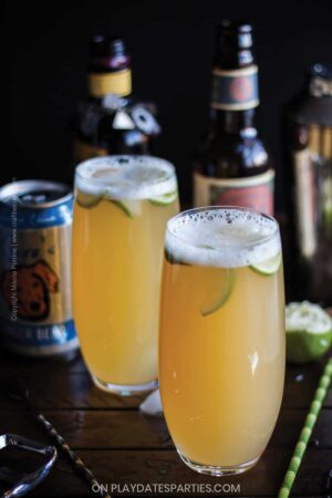 two beer cocktails garnished with lime in front of bottles of IPA
