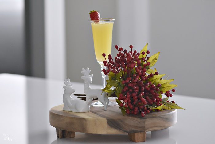 cocktail in a champagne flute sitting alongside a berry sprig and ceramic reindeer