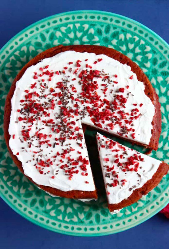 An overhead view of a red velvet cake with frosting and sprinkles on a teal plate