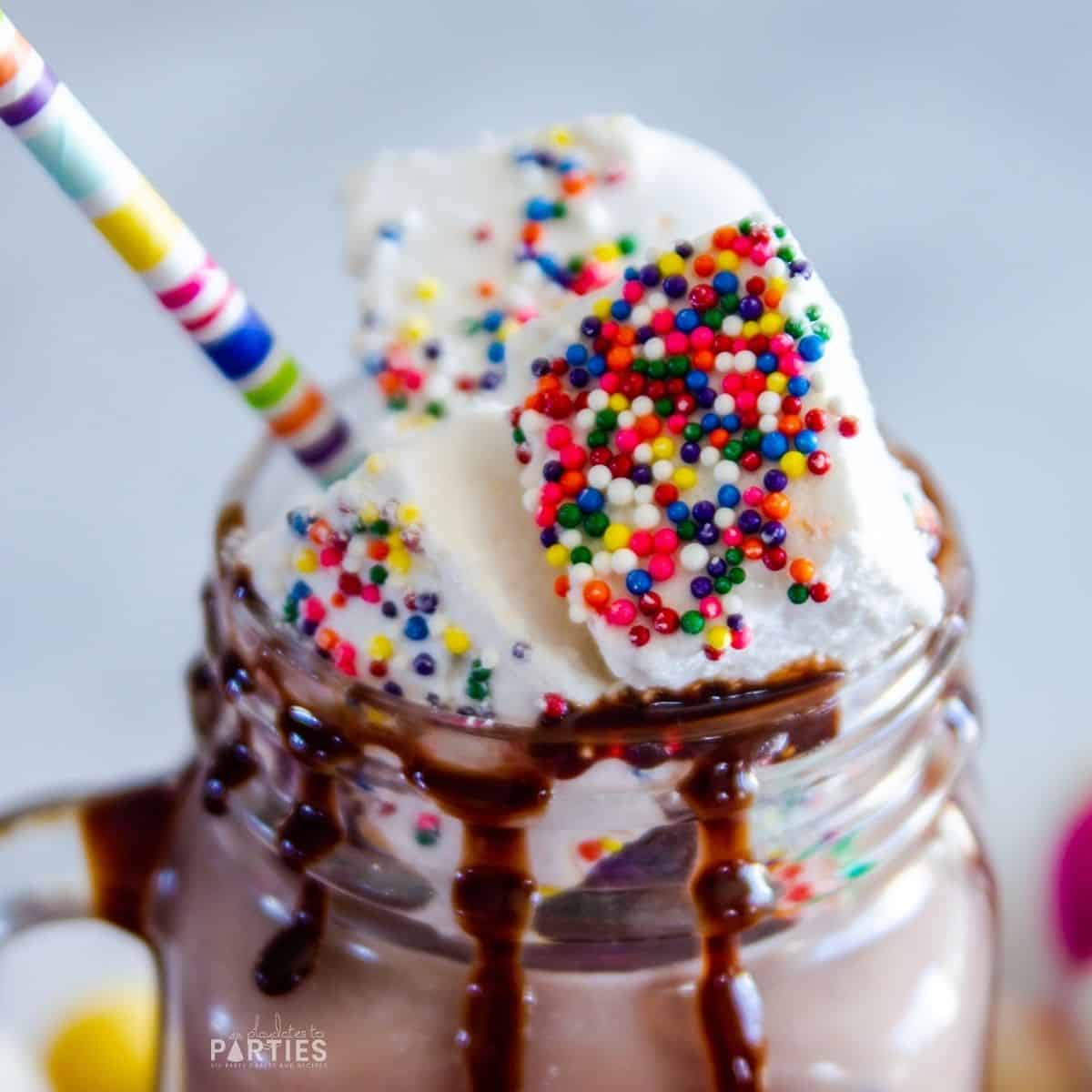 sprinkle coated marshmallows on top of a chocolate milkshake with a paper straw sticking out of it