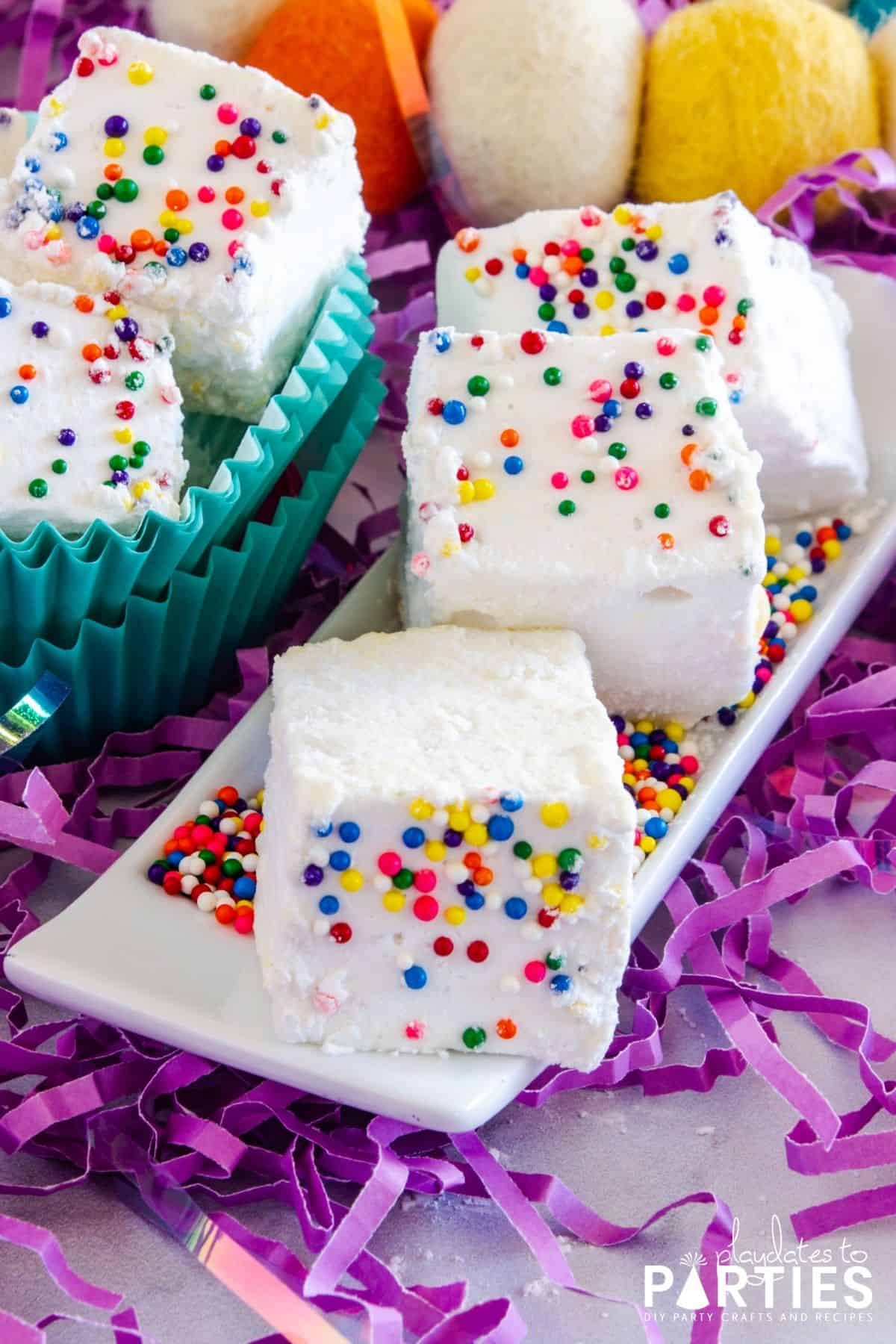 close up of homemade birthday cake marshmallows with sprinkles, on a white plate surrounded by purple confetti
