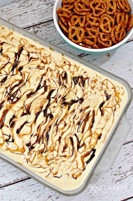 A 9x13 pan of ice cream cake with a bowl of pretzels next to it.