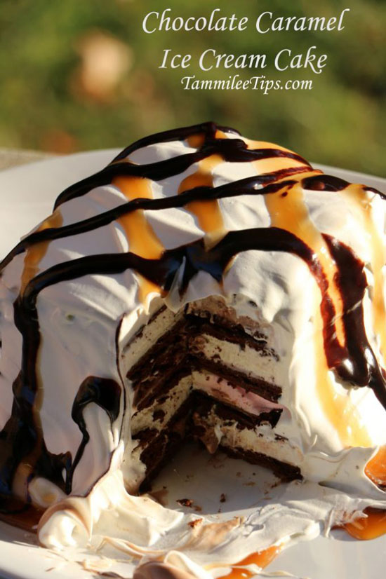 A layered ice cream cake with a section cut out to show the layers, with whipped topping and drizzles of chocolate and caramel on top.