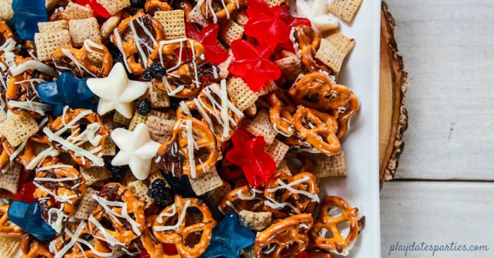 A plate of snack mix with chocolate drizzled pretzels, chex cereal, dried blueberries and gummy stars