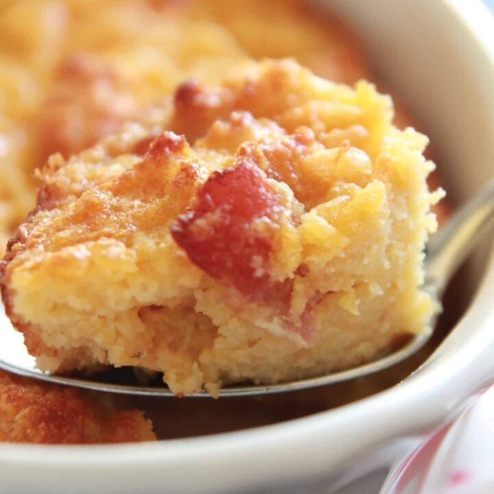 close up image of a spoon full of cornbread pudding with a large piece of bacon