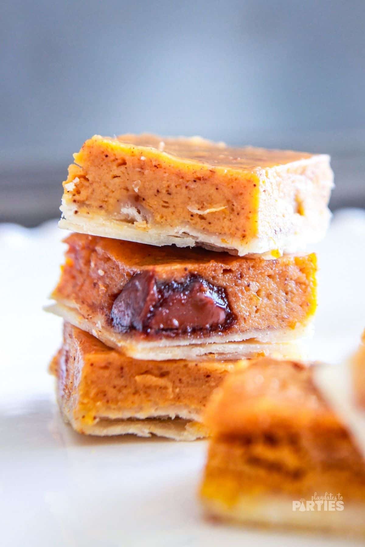 Three pumpkin pie bars with Nutella stacked on a white surface.
