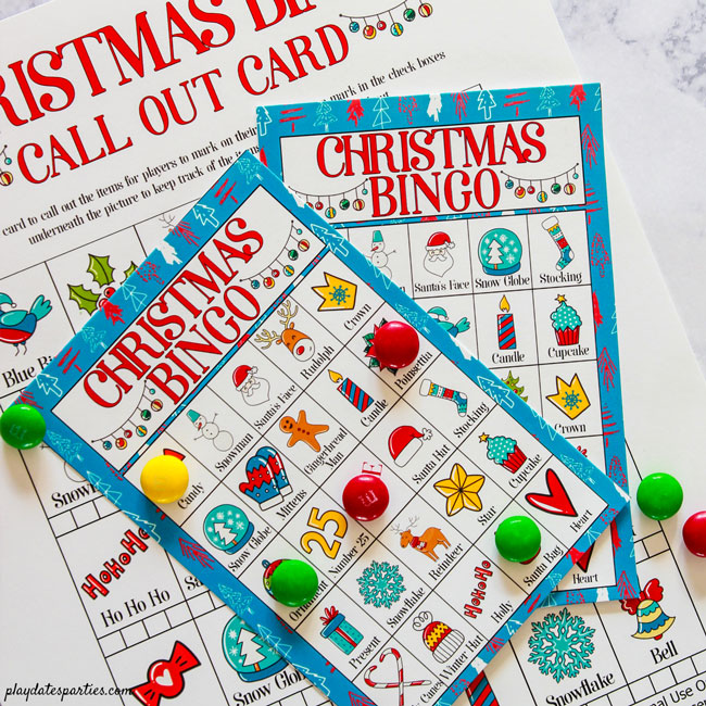 Call out page and two Christmas bingo cards on a marble counter with colorful candies as markers