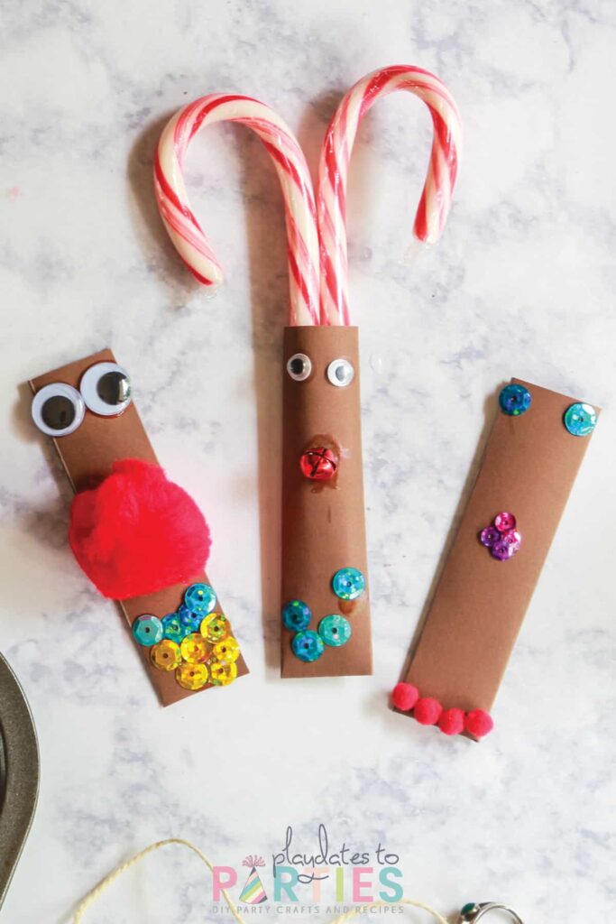 three brown pockets with faces made out of pom poms, sequins, and jingle bells. One pocket is made into a reindeer with candy canes as antlers