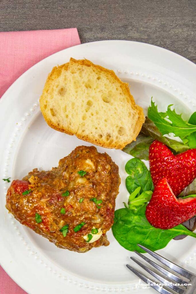 heart shaped meatloaf on a plate with heart shaped strawberries and salad