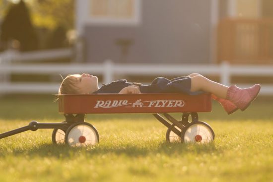 child laying in a red wagon on a sunny day