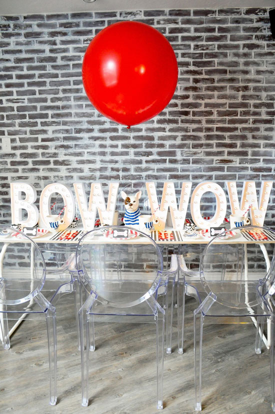 A dining table set up for a bulldog themed party with the words "Bow Wow" spelled in large marquee letters and a single red balloon floating above