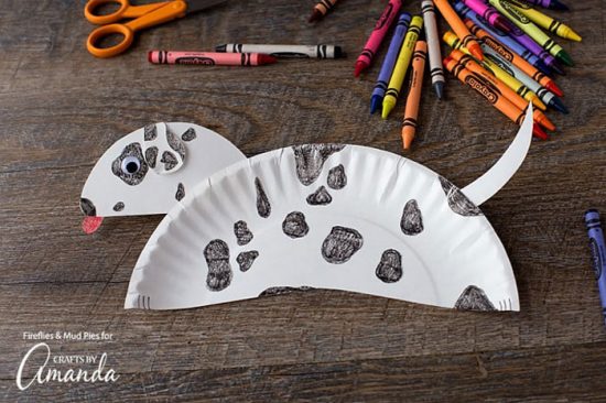 paper plate that looks like a puppy with black spots on a brown table next to crayons and scissors