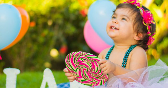 A picture of a toddler at a birthday party with a giant lollipop