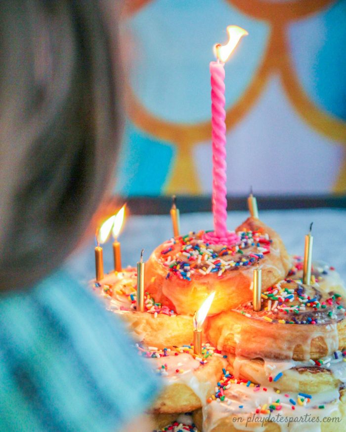 Child blowing out candles of a cinnamon roll cake for her birthday