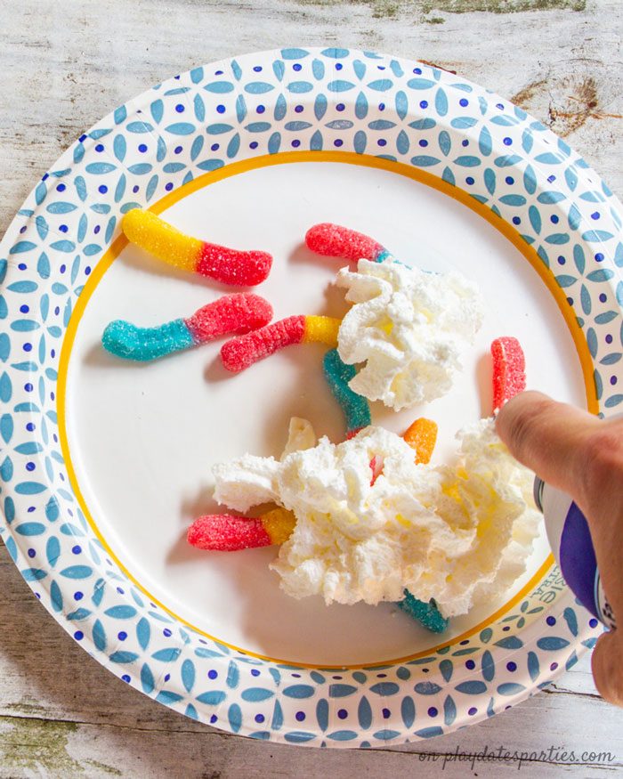 Covering gummy worms with whipped cream for a fun party game