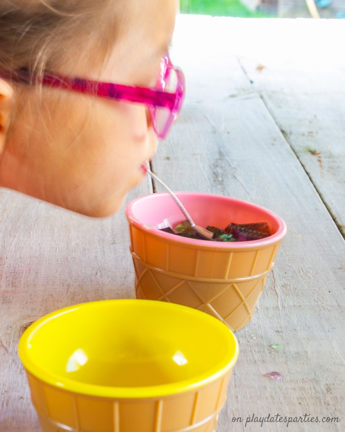 A girl holding a spoon in her mouth to move jello between cups in a minute to win it party game