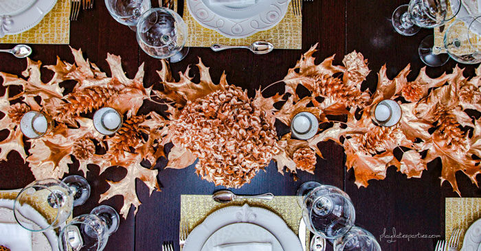 Overhead view of gold Thanksgiving decor on a table with gold leaves, pine cones, placemats, and gold flowers