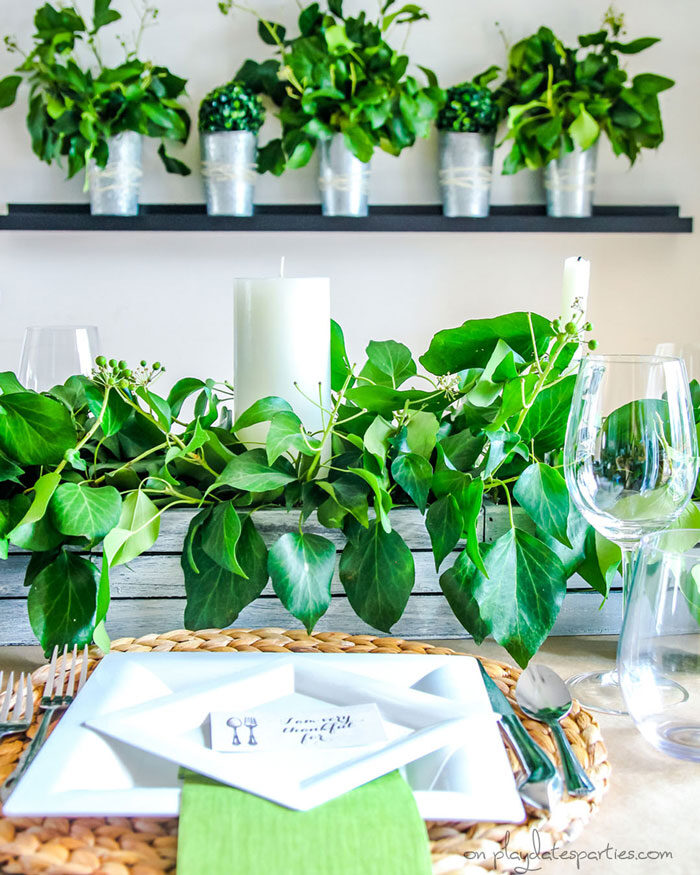 Fresh greenery on a Thanksgiving table and displayed in vases on the wall behind the table